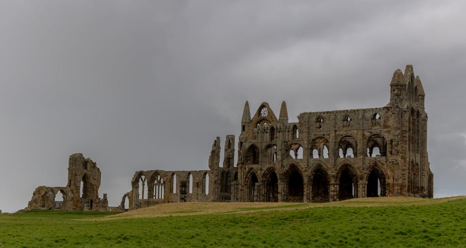 A stone ruin of a large historic building, possibly a cathedral or abbey, with multiple arched windows and doorways, some of which are partially collapsed or deteriorated. The structure features tall, pointed Gothic-style arches and vertical stone walls, set on a grassy hill under a cloudy, overcast sky. The ground surrounding the ruin is covered in green grass, with no visible vehicles, furniture, or moving equipment within the scene. This historic site provides a backdrop that could be associated with house removals or relocation services when considering the broader context of moving and transport logistics, as seen on the webpage titled 'Bulky item removal in Abbey Wood: fees & options' from Man With a Van Abbey Wood.